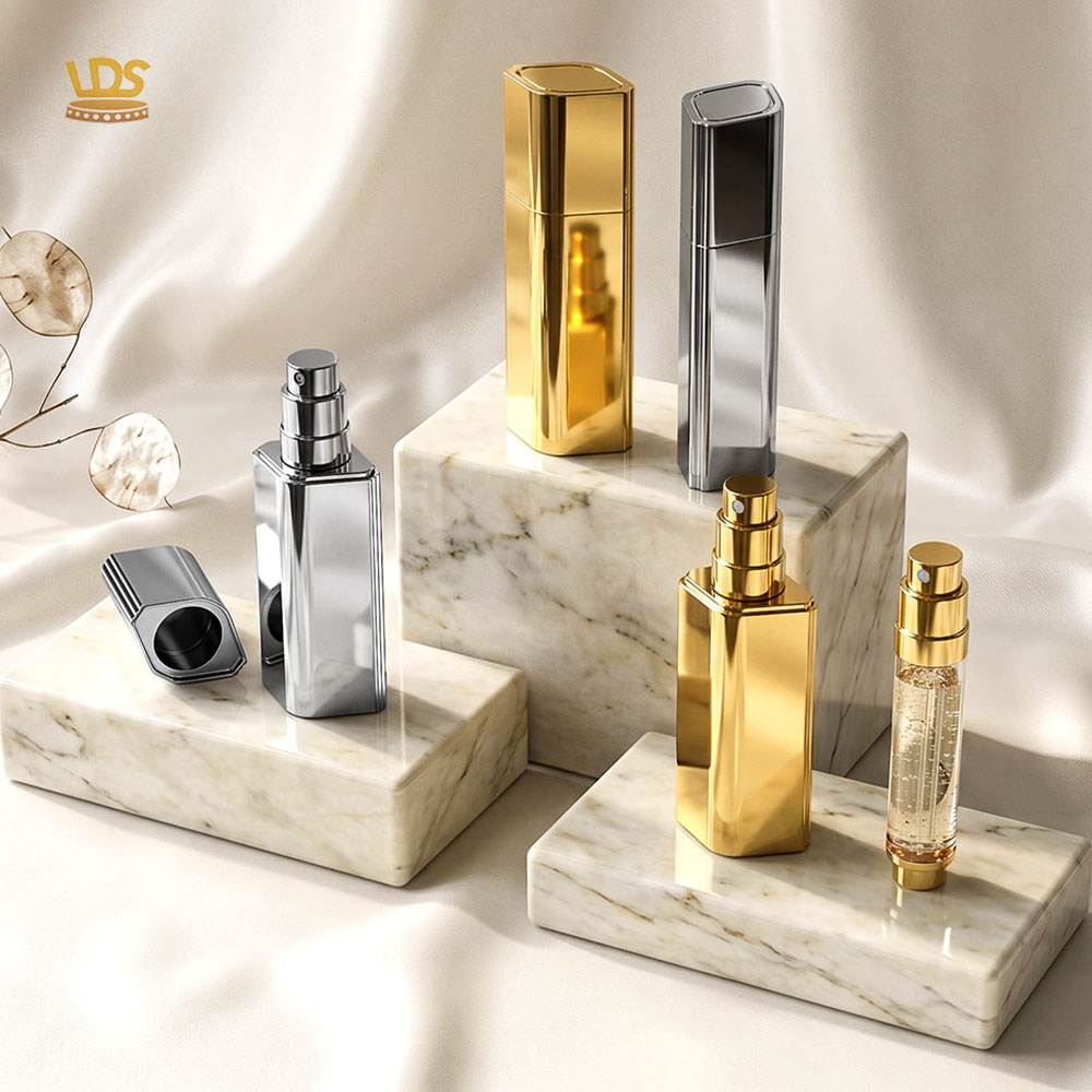Gold and silver rhombus magnetic travel spray perfume atomizers on marble display blocks with silk fabric backdrop.