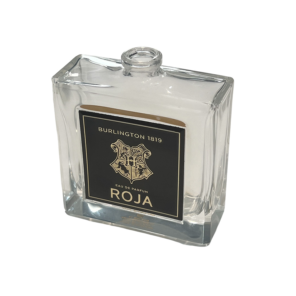 Clear glass perfume bottle featuring a custom black and gold square aluminum plaque label.