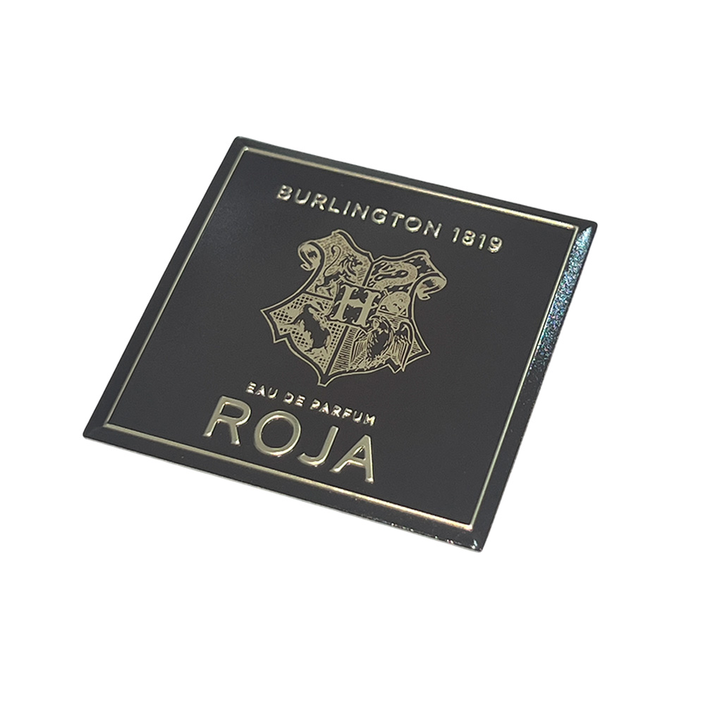 Close-up view of a custom square black aluminum plaque with embossed metallic gold logo and text.