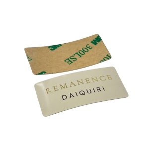 Vista frontal y posterior de una etiqueta de perfume de aluminio curvada personalizada que muestra el respaldo de cinta adhesiva 3M 300LSE.